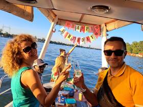 A joyful birthday celebration on a boat, with friends toasting cocktails and enjoying the beautiful waterfront view.