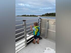 A young child in a life jacket gazes out over the water from the deck of a boat, capturing the essence of family adventures on the water.