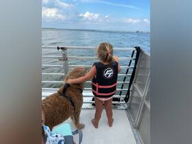 A young girl in a life jacket enjoys the view from a boat, accompanied by a friendly dog — a perfect moment of adventure on the water.
