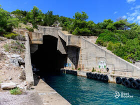 An unclear view of a concrete structure by the water, surrounded by greenery, possibly a dock or harbor entrance.