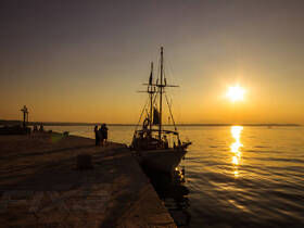 A picturesque sunset view featuring a group of people near a boat on the pier, creating a serene atmosphere perfect for evening outings.
