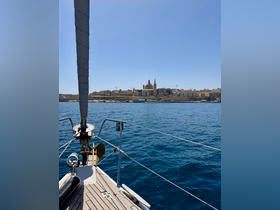 A stunning view from the bow of a sailboat, showcasing the beautiful coastline and architecture of a Mediterranean city under clear blue skies.