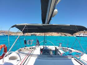 A view of the helm area inside a sailboat, showcasing the controls and shaded seating area against a backdrop of stunning turquoise waters.
