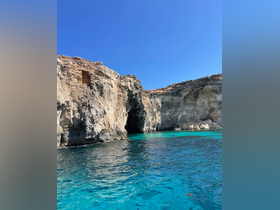 A stunning view of rocky cliffs and a cave along a beautiful coastline, surrounded by crystal-clear turquoise waters — a perfect destination for boating adventures.