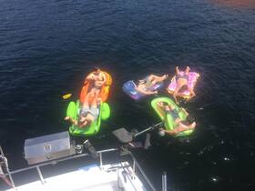 A group of friends relaxes on colorful floaties in the water, enjoying a sunny day on the boat — perfect for summer fun and relaxation.