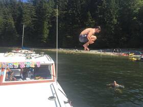 A man leaps off a boat into the water during a birthday celebration, surrounded by friends enjoying a sunny day at the beach. Perfect for capturing fun moments on the water.