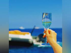A hand raises a glass of champagne against the backdrop of a boat on the ocean, capturing the essence of celebration and luxury on the water.
