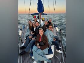A cheerful group enjoys a sailing trip at sunset, sipping cocktails and wrapped in cozy blankets, creating a perfect atmosphere for celebration on the water.