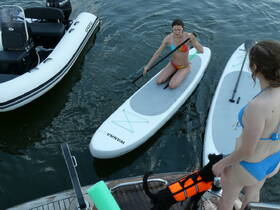 Two friends enjoy paddleboarding on the water, accompanied by a dog in a life jacket — a perfect day for water activities and fun in the sun.