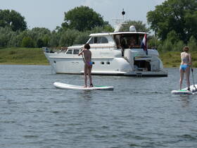 Two young girls enjoy paddleboarding in front of a luxurious boat on a sunny day, showcasing the perfect summer water activity.
