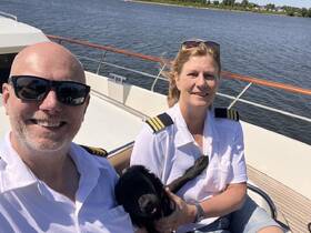 A smiling couple enjoys a sunny day on a boat with their dog, showcasing the joy of boating adventures together.