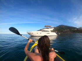 A kayaker paddles towards a luxurious yacht, surrounded by serene waters and stunning scenery — perfect for adventure seekers and water enthusiasts.