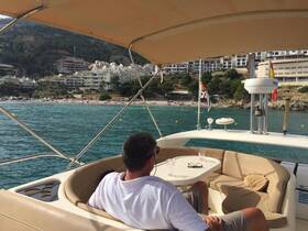 A man relaxes on the deck of a boat, enjoying the scenic view of a beach and coastal buildings — a perfect setting for a leisurely day on the water.