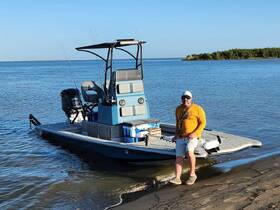 A man stands beside a fishing boat on the shore, ready for a day of adventure on the water. Perfect for fishing enthusiasts looking to explore the great outdoors.