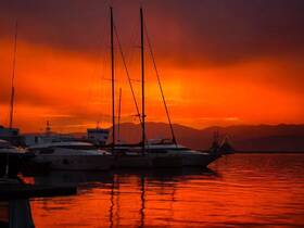 A stunning sunset casts vibrant orange hues over yachts docked at the marina, creating a picturesque scene perfect for evening reflections.