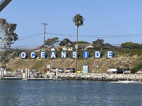 A scenic view of the Oceanside sign with people enjoying the harbor area, capturing the essence of coastal life.
