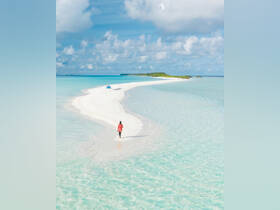 A solitary figure walks along a stunning sandbar surrounded by crystal-clear turquoise waters, showcasing the beauty of tropical destinations.