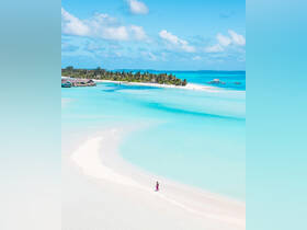 A serene beach scene featuring a person walking along the shore, surrounded by stunning turquoise waters and lush island greenery — a perfect representation of tropical paradise.