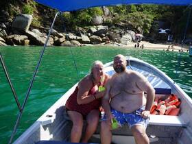 A cheerful couple enjoys drinks on a boat, with a scenic beach backdrop — perfect for a relaxing day on the water.