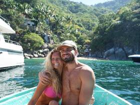 A happy couple poses for a photo on a small boat in a tropical setting, capturing the essence of a joyful vacation experience.