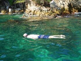 A snorkeler glides through crystal-clear waters near a rocky coastline, showcasing the beauty of underwater exploration.