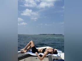 A young woman relaxes on the bow of a boat, soaking up the sun and enjoying the serene ocean views — a perfect moment for relaxation on the water.