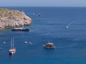 A stunning aerial view of multiple boats navigating through crystal-clear waters near a rocky coastline, showcasing the beauty of a vibrant marine landscape.