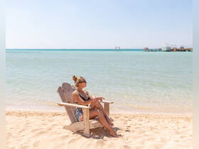 A woman relaxes on a beach chair by the turquoise waters, enjoying the serene ocean view — a perfect spot for unwinding and soaking up the sun.