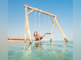 A woman enjoys a serene moment swinging over clear waters, capturing the essence of relaxation at the beach — a perfect spot for memorable vacation photos.