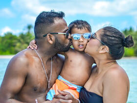 A joyful family moment captured as parents kiss their son in a beautiful beach setting, perfect for celebrating love and togetherness under the sun.