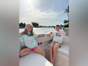 Two children enjoy a sunny day on a boat, smiling and relaxing by the water — a perfect family outing on the water.