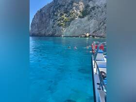 A group enjoys swimming in the crystal-clear waters near a stunning rocky coastline, showcasing the beauty of a perfect day on the water.