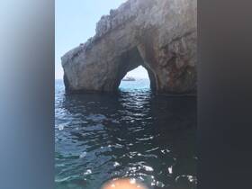 A stunning view of a boat passing through a natural rock arch, showcasing the beautiful coastline and crystal-clear waters — perfect for scenic boat tours.