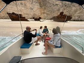 A group of friends enjoys a boat trip near a famous shipwreck on a sandy beach, capturing the moment with stunning scenery in the background.