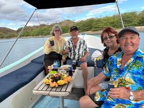 A cheerful group enjoys cocktails and a delicious spread of fruits aboard a boat, perfect for a relaxing day on the water.