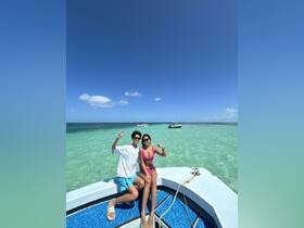 A cheerful couple poses on the bow of a boat, enjoying a sunny day on clear turquoise waters — perfect for romantic getaways or fun adventures on the sea.