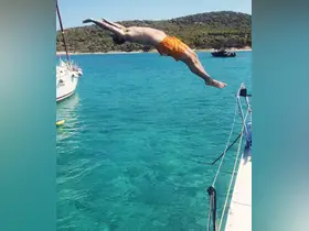 A man leaps off the side of a sailboat into the crystal-clear waters, capturing the thrill of summer adventures on the water.