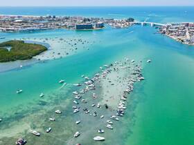 A vibrant aerial view of a busy sandbar filled with boats and people enjoying the water, showcasing the lively atmosphere of a popular boating destination.