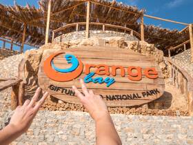 A close-up of hands making peace signs in front of the Orange Bay sign at Giftun Island National Park, capturing a moment of excitement at this popular destination.