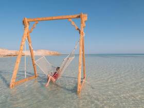 A serene scene of a woman relaxing in a hammock on the beach, surrounded by clear waters — an ideal spot for unwinding and enjoying the beautiful scenery.