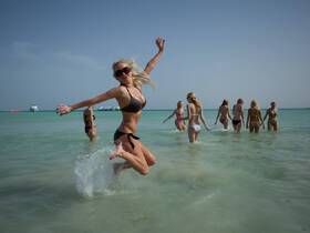A lively group of women enjoys a fun day at the beach, splashing in the water and celebrating together — perfect for summer adventures and beach parties.