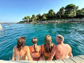 A joyful group enjoys a sunny day by the water, sitting on the edge of a boat and taking in the beautiful scenery — perfect for family outings and beach adventures.