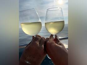 Two glasses of white wine clink together against a serene backdrop of the sea, capturing a moment of celebration on the water — perfect for romantic evenings or special occasions.
