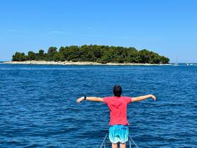 A young boy stands at the bow of a boat, arms outstretched, enjoying the stunning view of a lush island in the distance — a perfect moment of joy on the water.
