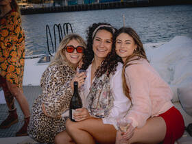 A joyful group of friends enjoys a celebration on a boat, toasting with cocktails and capturing memorable moments together.