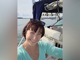 A woman smiles for a selfie on a boat, showcasing the serene waters and a glimpse of the shoreline in the background — perfect for capturing joyful moments on the water.