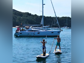 Two children paddleboard in clear waters near a sailboat, capturing the essence of summer fun and adventure on the water.