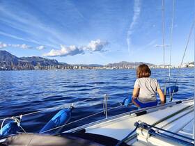 A child enjoys the view from a sailboat, overlooking a stunning cityscape and mountains — a perfect moment of adventure on the water.