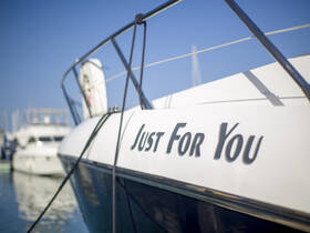 Close-up view of a boat named 'Just For You' docked in a marina, showcasing its sleek design against a clear blue sky.