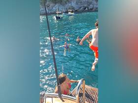 A lively scene of guests enjoying a refreshing swim, with one person jumping from the boat into the clear blue waters — perfect for summer adventures and group fun on the water.